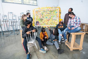 Students gather around easels and canvas for a studio art critique session