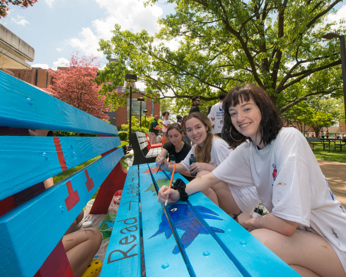 Students paint a bench on the quad between Fenwick and Sub1 with bright colors and Dr. Seuss inspired graphics