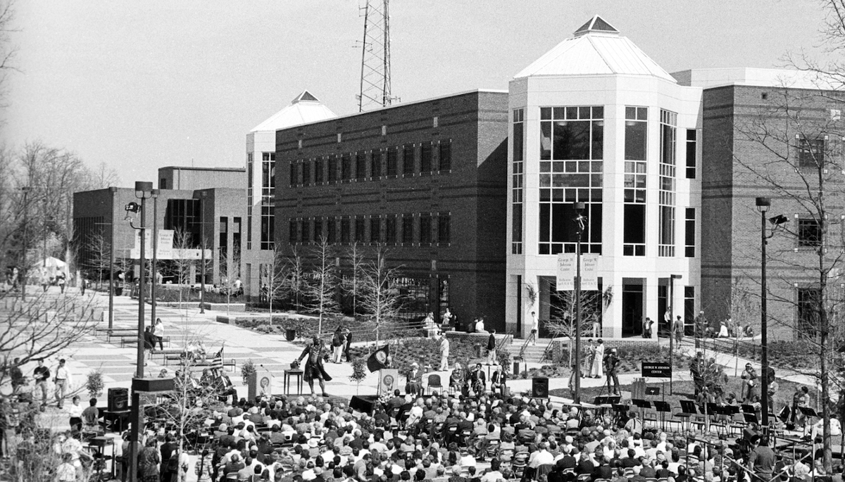 black and white photo of people sitting on folding chair outside of a brick building