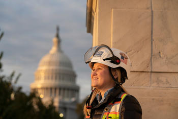 Happy looking woman in hard-hat observes the sunset while standing in front of the U.S. Capitol rotunda.