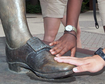 Close up of hands touching the burnished bronze toe of the George Mason Statue for "good luck" as the tradition holds.